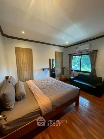Spacious bedroom with wooden flooring, large window, and cozy seating area.