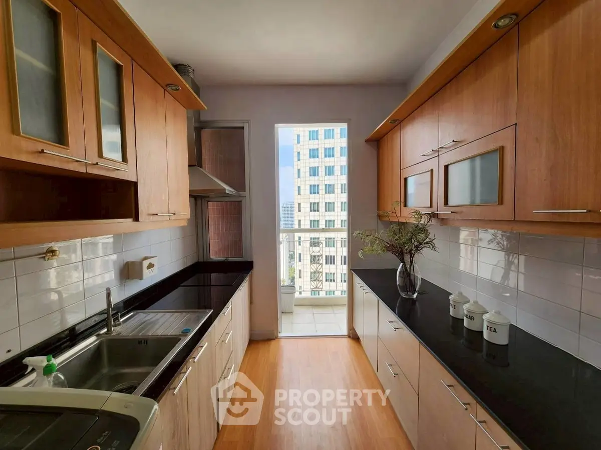 Modern kitchen with sleek black countertops and wooden cabinets, offering a bright view of the cityscape.