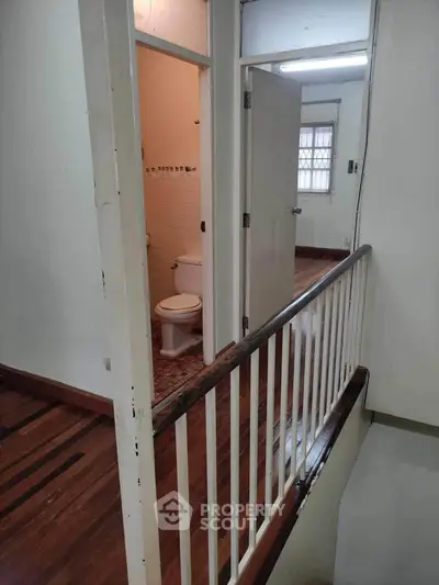 Spacious interior hallway leading to a bathroom and room, featuring wooden flooring and white walls.