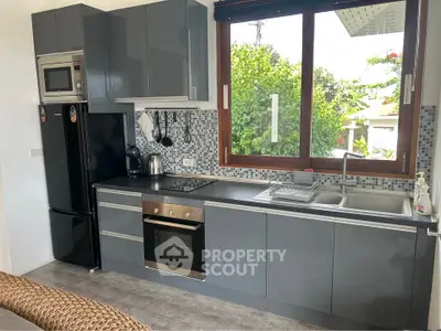 Modern kitchen with sleek cabinetry, built-in oven, and large window overlooking lush greenery.
