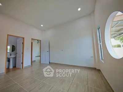 Spacious unfurnished room with modern tile flooring and round window, ideal for customization.