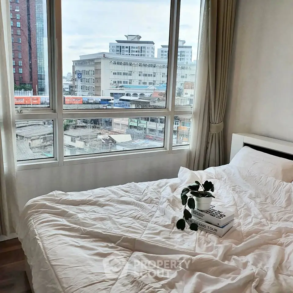 Cozy bedroom with city view, featuring a comfortable bed and large windows for natural light.