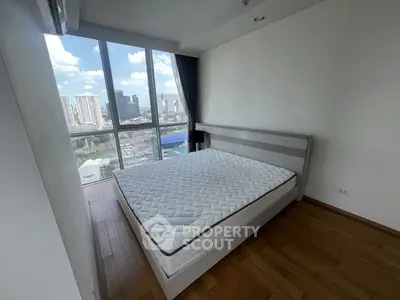 Spacious bedroom with large window offering stunning city views, featuring a comfortable bed and wooden flooring.
