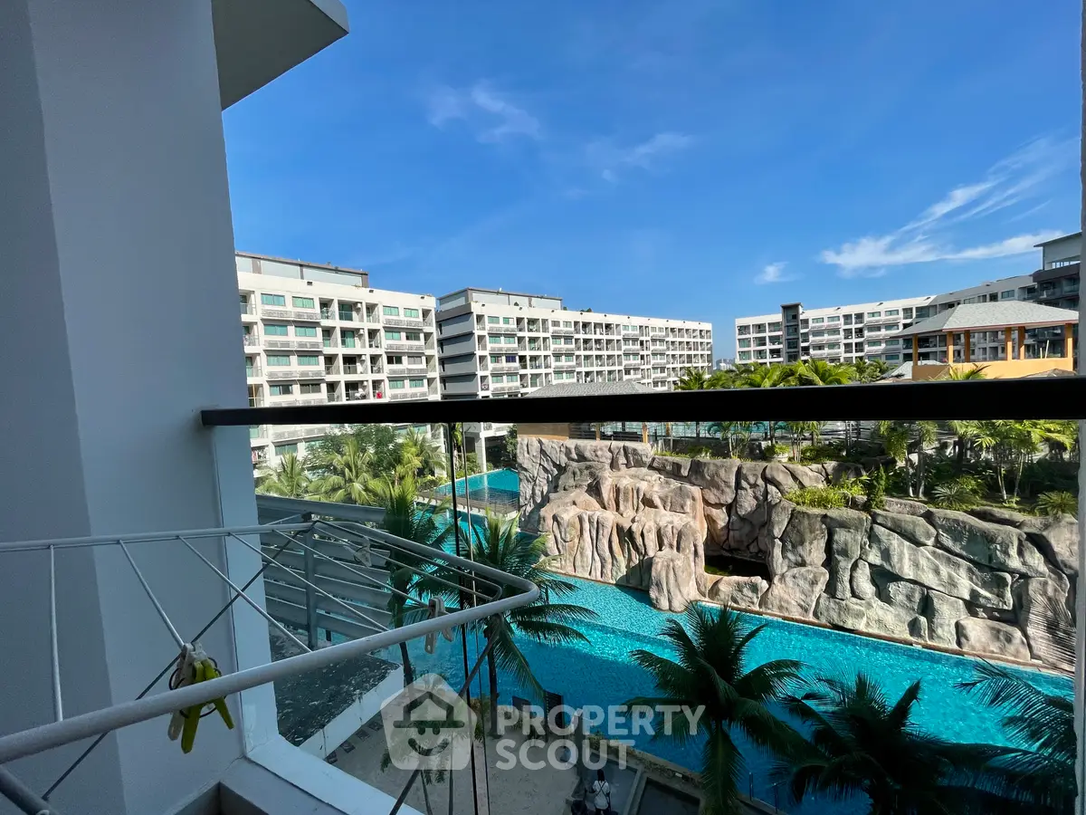 Stunning balcony view of resort-style pool and modern apartment buildings under clear blue sky.