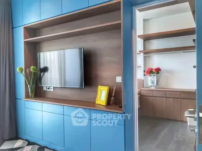 Modern living room with built-in TV unit and adjacent walk-in closet, featuring sleek blue cabinetry.