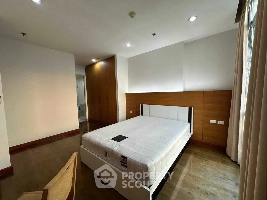 Spacious bedroom with modern design and ample natural light, featuring a comfortable bed and stylish wooden accents.