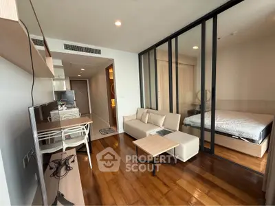 Modern studio apartment with glass partition, wooden flooring, and sleek furniture design.