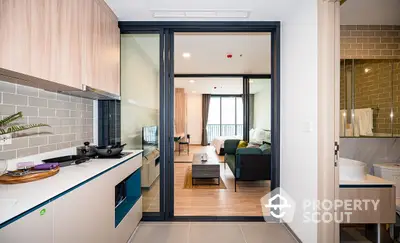 Modern apartment with an open layout kitchen featuring sleek countertops and a view into a cozy living room with ample natural light and a comfortable ambiance.