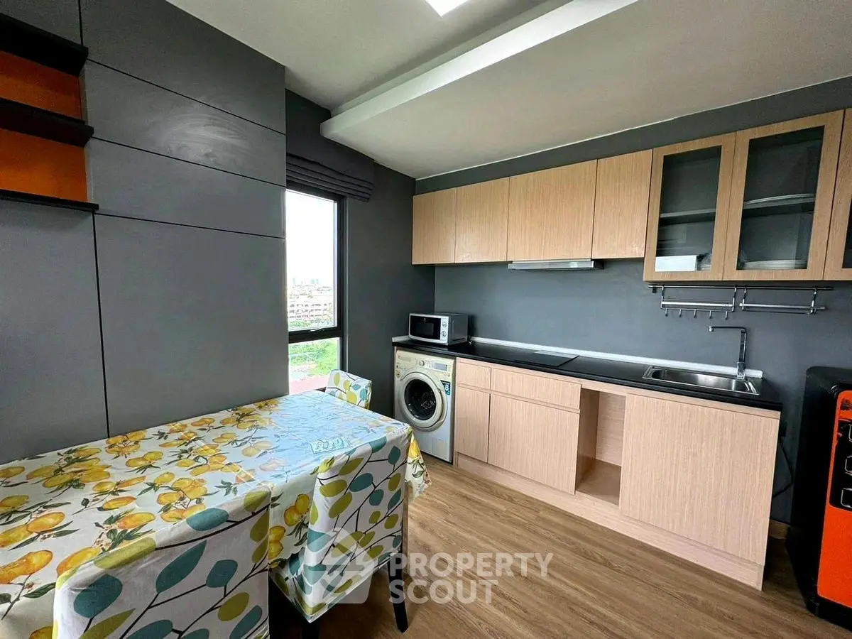 Modern kitchen with washing machine and dining area, featuring sleek cabinetry and vibrant tablecloth.