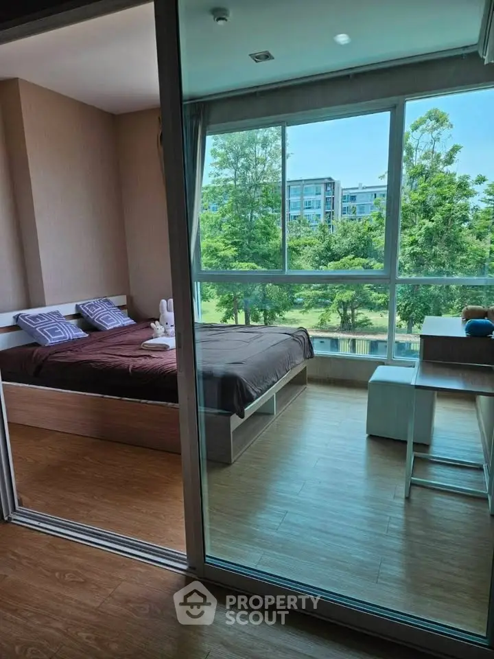 Modern bedroom with large windows offering a serene view of greenery, featuring stylish decor and wooden flooring.