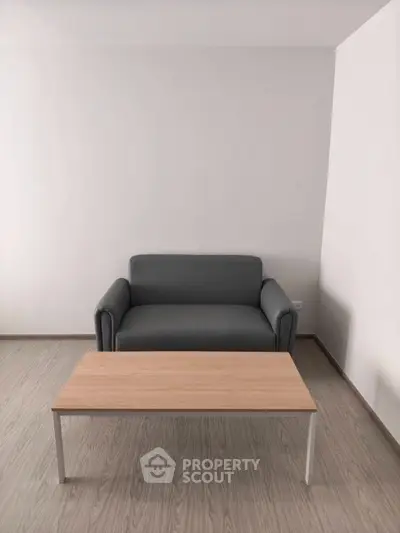 Minimalist living room with a sleek gray sofa and wooden coffee table on light wood flooring.