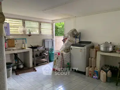 Spacious kitchen with washing machine and ample storage space, featuring a tiled floor and large windows for natural light.