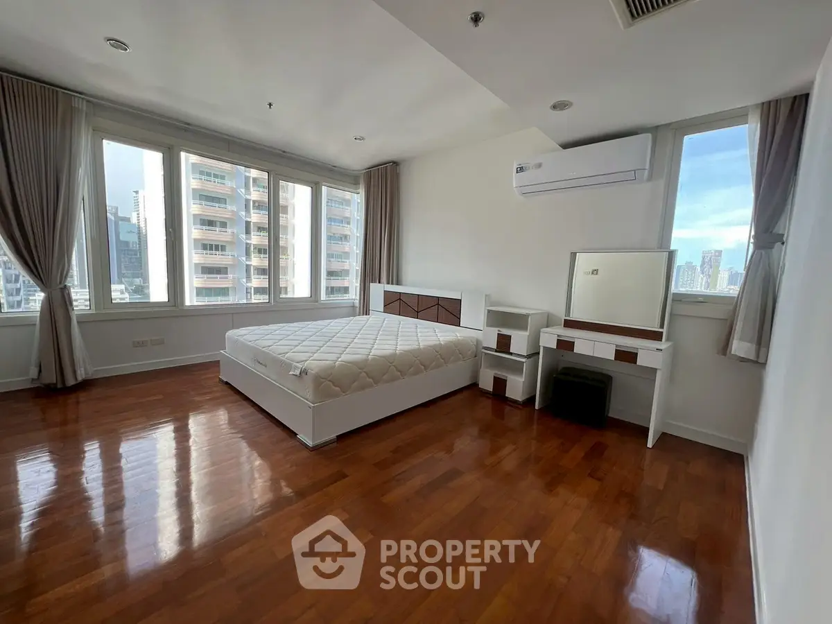 Spacious bedroom with city view, featuring hardwood floors and modern furnishings.
