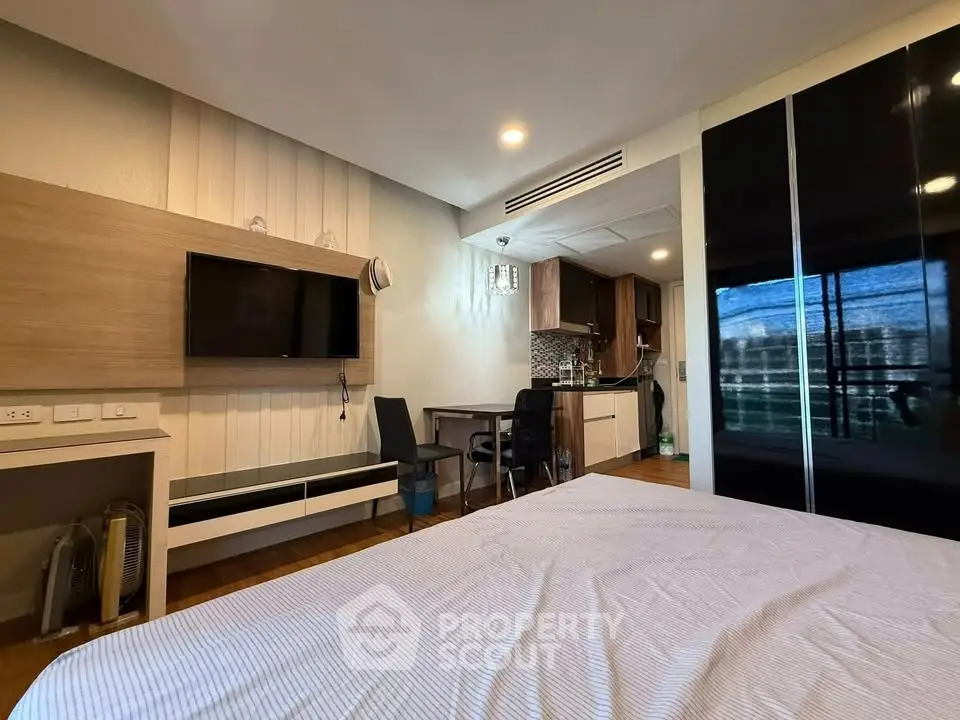 Modern bedroom with sleek TV setup and stylish kitchen area in open layout apartment.