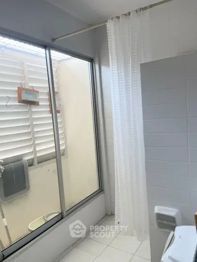 Bright bathroom with large window and white curtain, offering natural light and privacy.