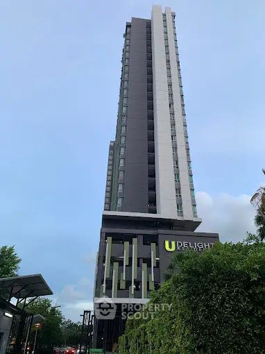 Modern high-rise building with sleek design and lush greenery at entrance.