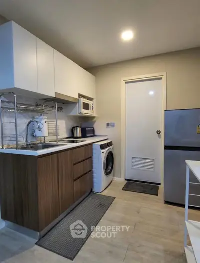 Modern kitchen with washing machine, fridge, and microwave in compact layout.