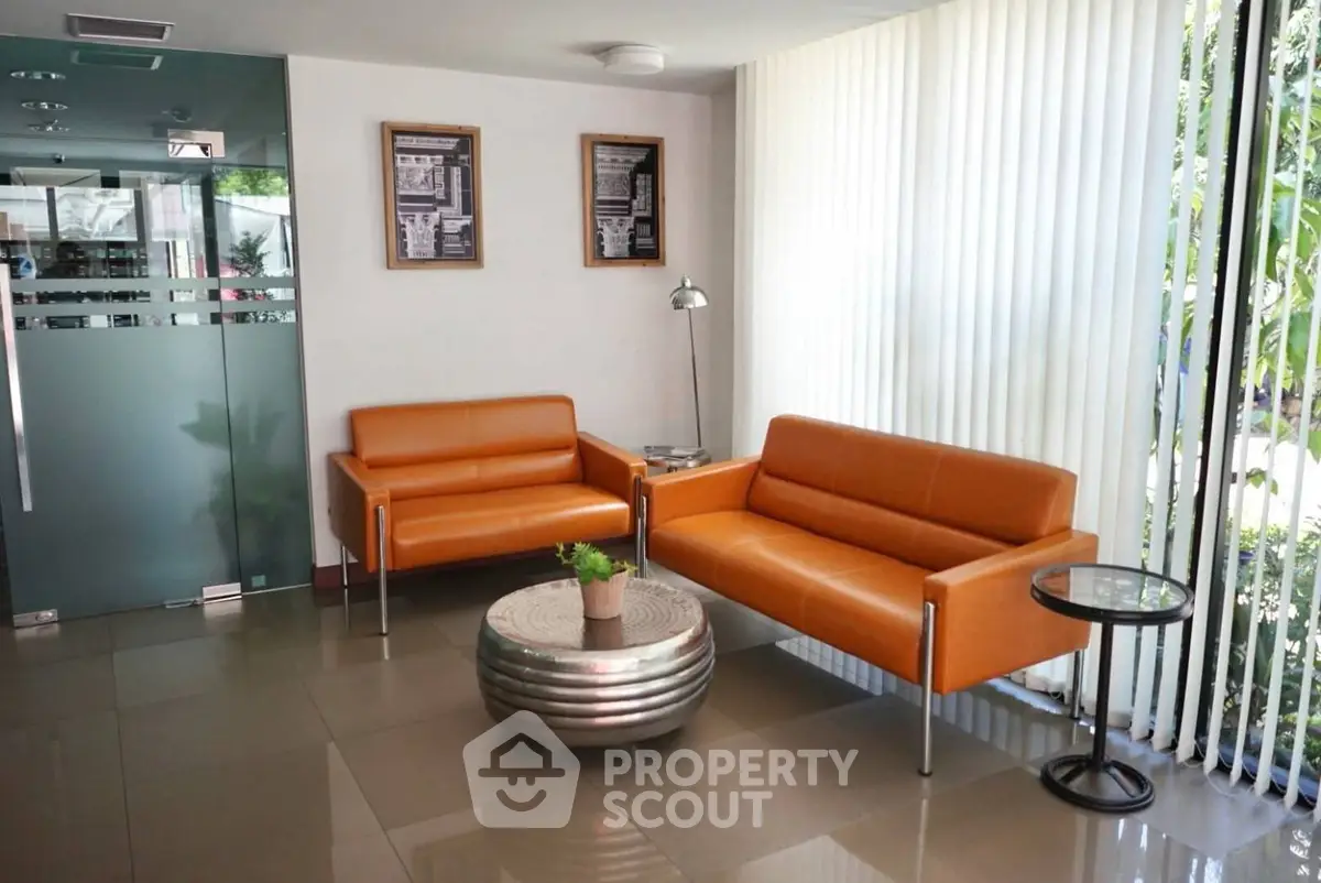 Modern office lobby with orange sofas and glass door, featuring sleek decor and natural light.