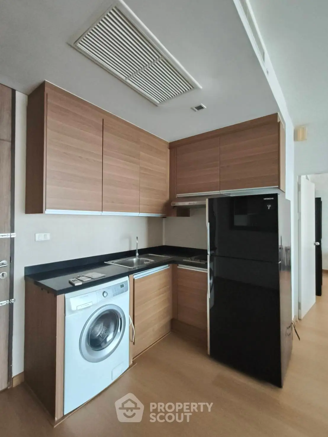 Modern kitchen with sleek wooden cabinets, black countertops, and built-in appliances including a washing machine.