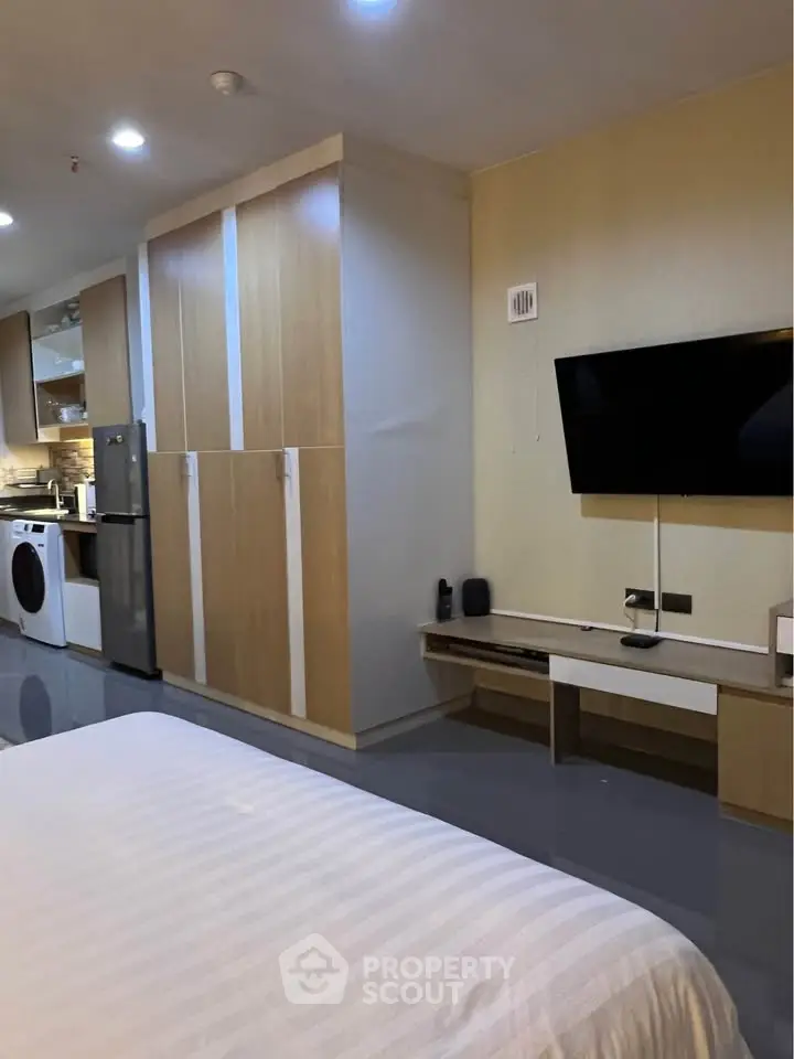 Modern studio apartment with sleek kitchen and cozy living area, featuring a wall-mounted TV and ample storage.