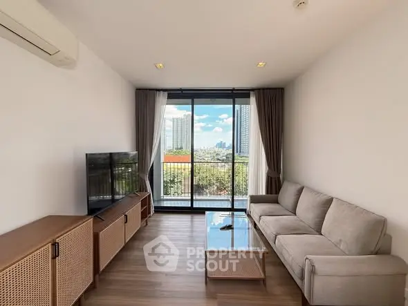 Modern living room with balcony and city view, featuring sleek furniture and natural light.