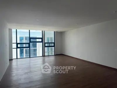 Spacious empty living room with large windows and wooden flooring in modern apartment.