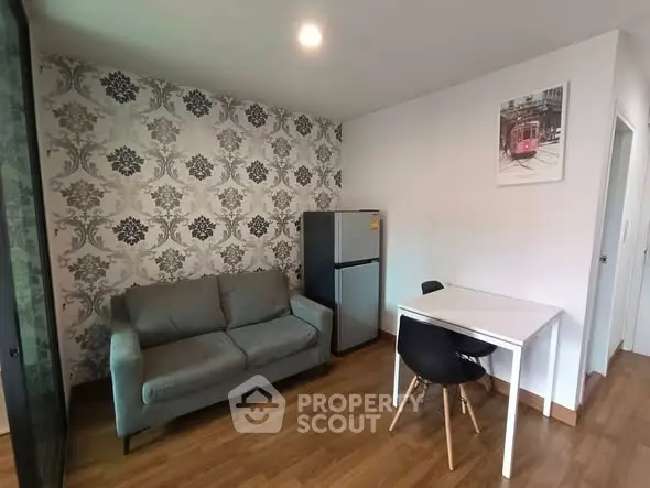 Modern living room with stylish wallpaper, compact fridge, and cozy seating area.