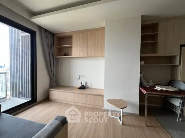 Modern living room with wooden flooring and built-in storage, featuring a large window with city view.