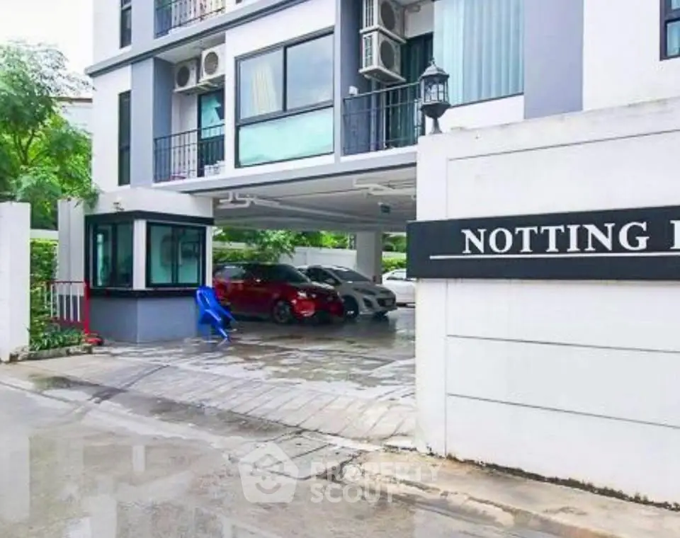 Modern apartment building entrance with parking area and security booth.