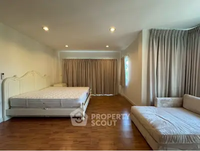 Spacious bedroom with elegant bed and cozy seating area, featuring wooden flooring and ample natural light.
