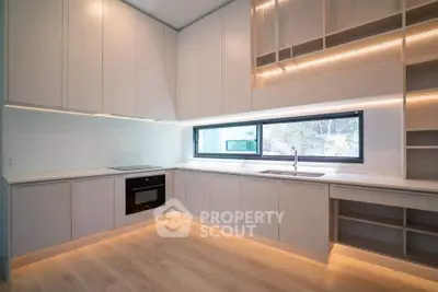 Modern kitchen with sleek cabinetry and built-in oven, featuring under-cabinet lighting and large window.