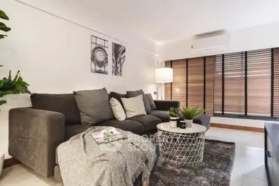 Stylish modern living room with cozy gray sofa, chic decor, and large windows with blinds.