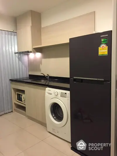 Modern kitchen with sleek black refrigerator, built-in oven, and washing machine, complemented by warm lighting and ample storage space.