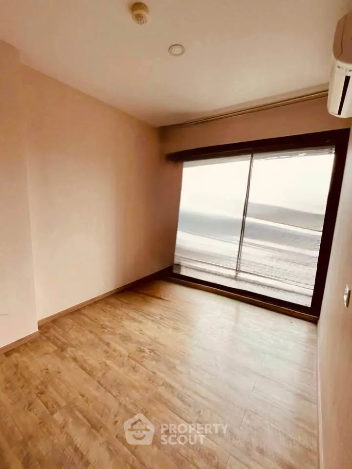 Spacious room with wooden flooring and large window offering natural light