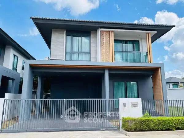 Modern two-story house with sleek design and gated entrance under a clear blue sky.