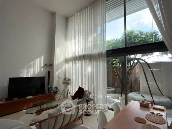 Spacious living room with high ceilings and large windows offering natural light and garden view.