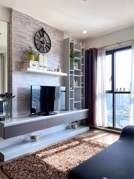 Modern living room with stylish decor and city view, featuring a sleek TV unit and large window.
