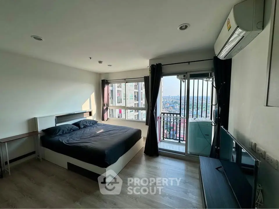 Modern bedroom with large windows and balcony offering stunning city views, featuring sleek furnishings and natural light.