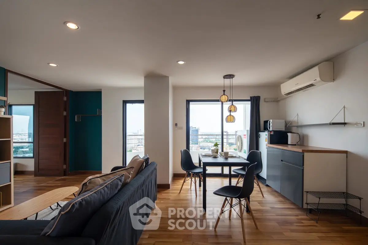 Modern open-plan living room with dining area and city view, featuring sleek furniture and wooden flooring.