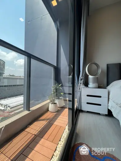 Modern bedroom with floor-to-ceiling windows and small balcony offering city views.