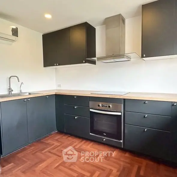 Modern kitchen with sleek black cabinets and built-in oven in stylish apartment.