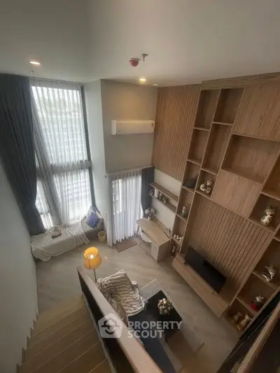 Modern loft-style living room with high ceilings and large windows, featuring stylish wooden shelving and cozy seating area.