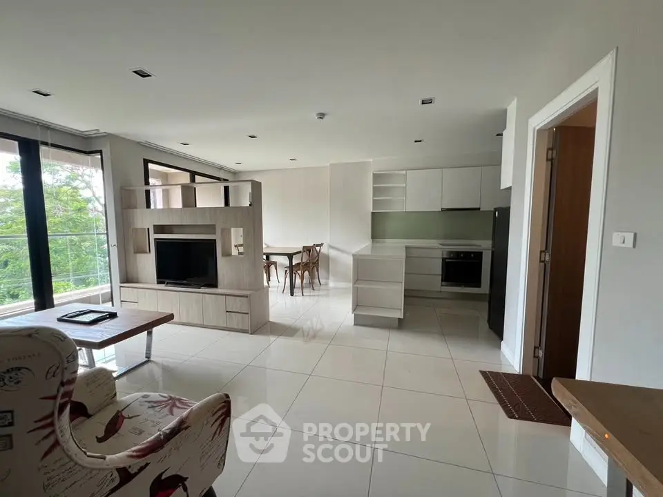 Spacious open-plan living room with modern kitchen and dining area, featuring large windows and stylish decor.