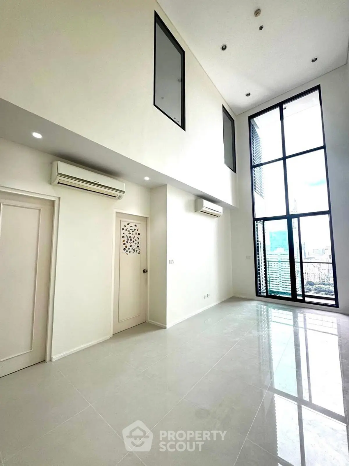 Spacious modern living room with high ceilings and large windows offering city views.