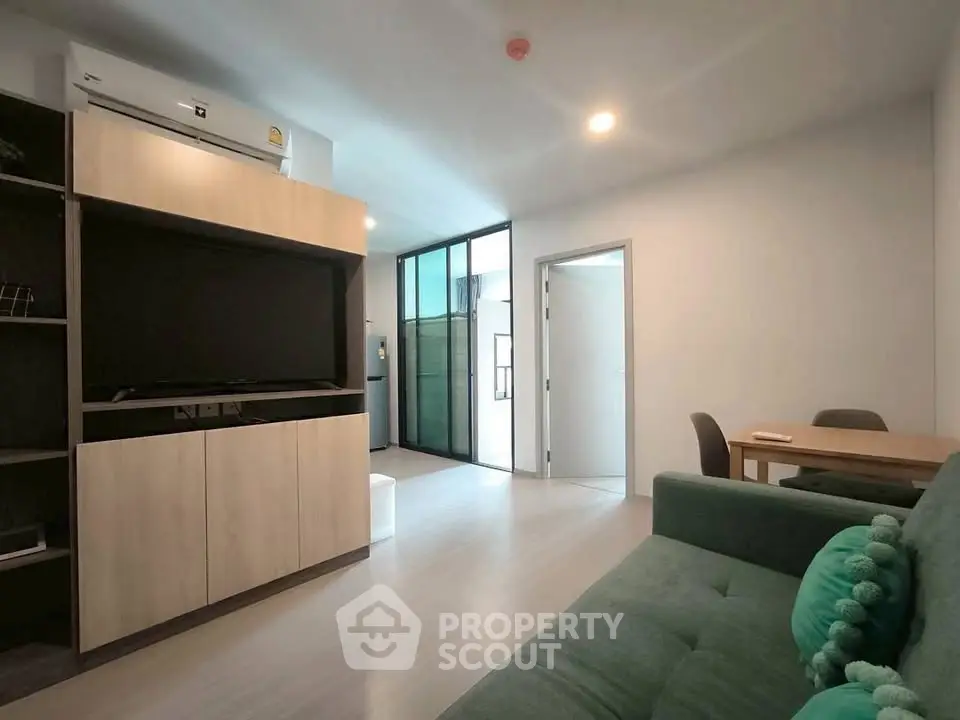 Modern living room with sleek furniture and open layout, featuring a cozy green sofa and dining area.