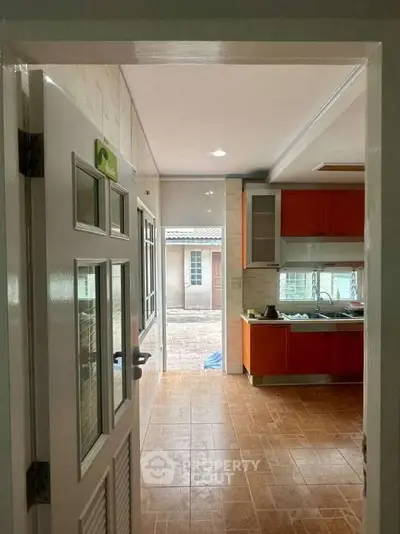 Charming kitchen with orange cabinets and tiled floor, leading to a bright outdoor area.