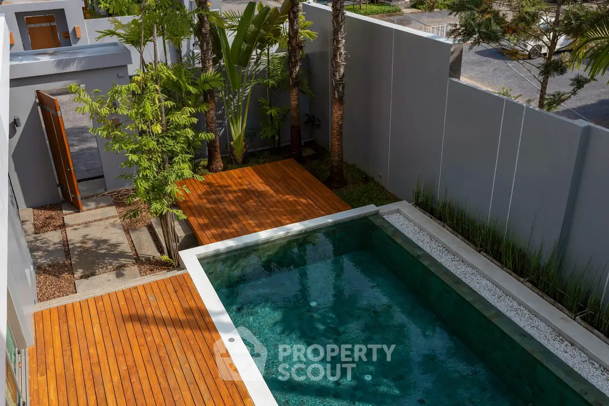 Luxurious private pool with wooden deck and lush greenery in modern backyard.