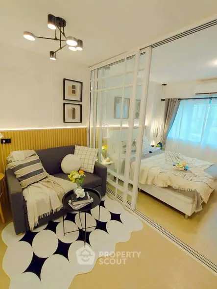 Modern studio apartment with stylish living area and cozy bedroom separated by glass partition.