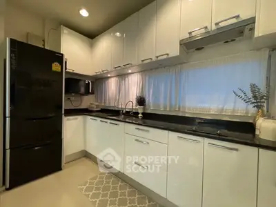 Modern kitchen with sleek white cabinets and black countertops, featuring a large fridge and microwave.