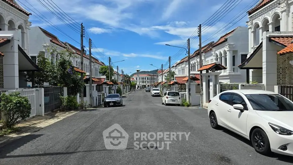 Charming residential street with white houses and red roofs under a clear blue sky.